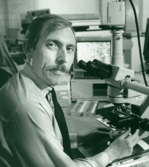 Photo of professor Andrew P. Zalewski sitting at a desk working with a microscope.