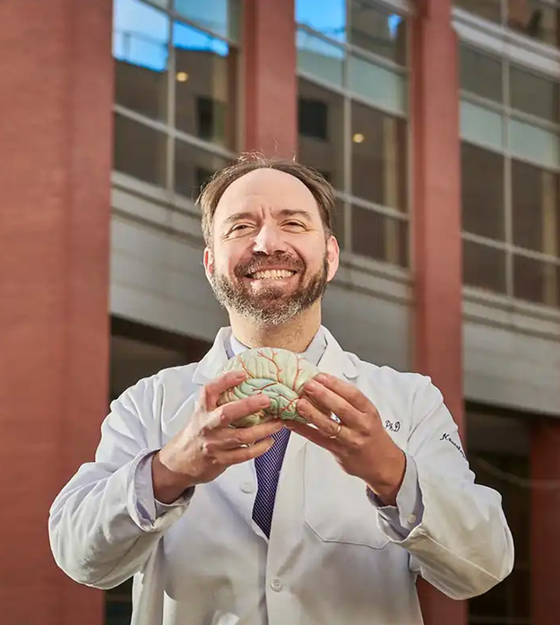 A doctor holding a model of a brain outside of a building.