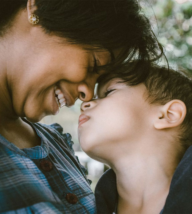 A woman with her eyes closed wears a plaid, button-up top and smiles while touching her forehead to a child’s forehead. The child also has their eyes closed and wears a dark hooded sweatshirt. Photo by Bruno Nascimento on Unsplash.