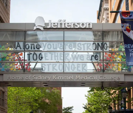 Jefferson logo on Home of Sidney Kimmel Medical College building with a sign in the window reading "Alone you are STRONG TOGETHER we are STRONGER"