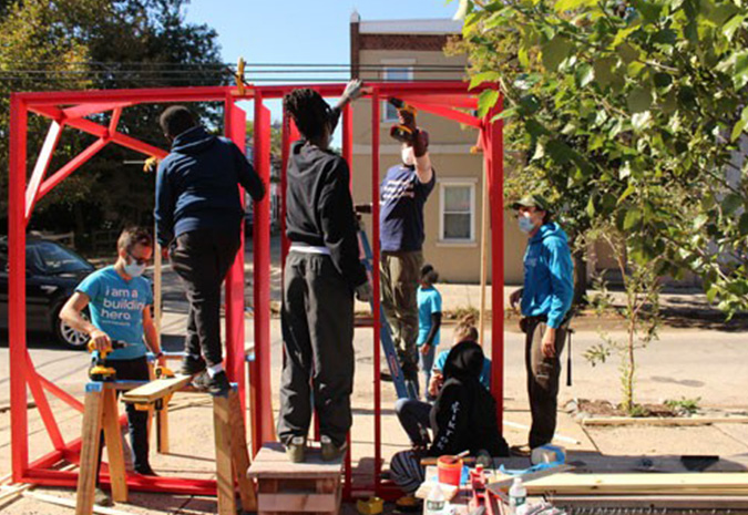 A group of workers construct a red canopy during a Park in a Truck installation on the corner of an empty city lot.