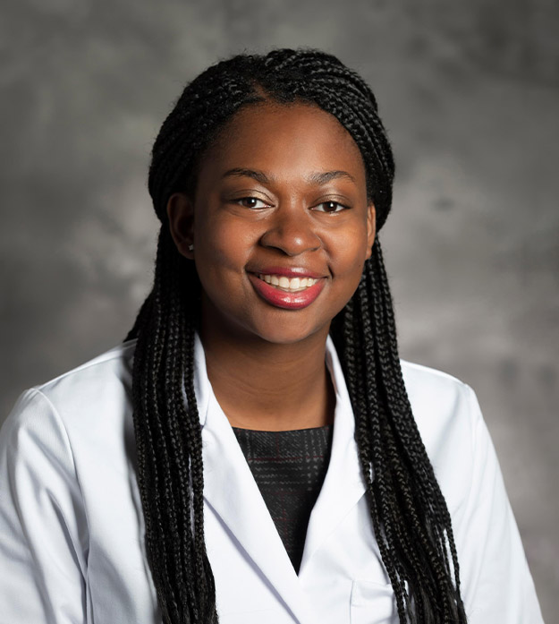 Lauren Coaxum wears a white lab coat over a formal black top while smiling at the camera in a professional headshot pose.