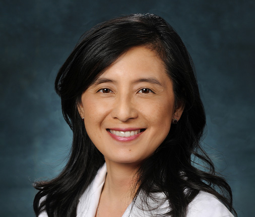 Dr. Grace Lu-Yao wears a formal shirt and her hair down past her shoulders while smiling at the camera in a professional headshot pose.