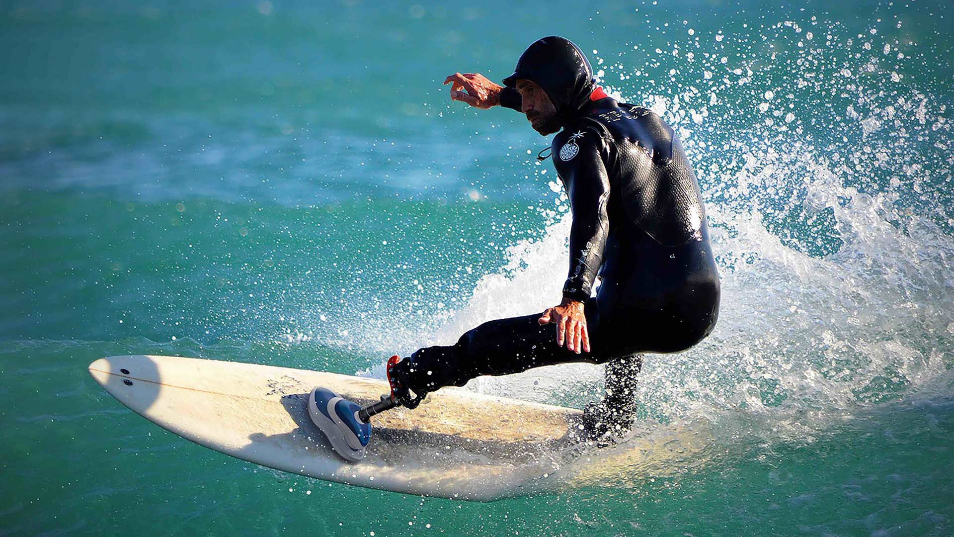 A surfer catches a wave while wearing a black, full-body wetsuit and a rendering of the Swell Surf Foot prosthetic.