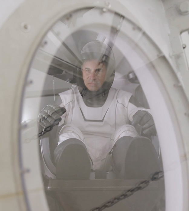 Eytan Stibbe, an Israeli astronaut who completed the Rakia Mission, is seen through a window wearing a spacesuit and helmet.