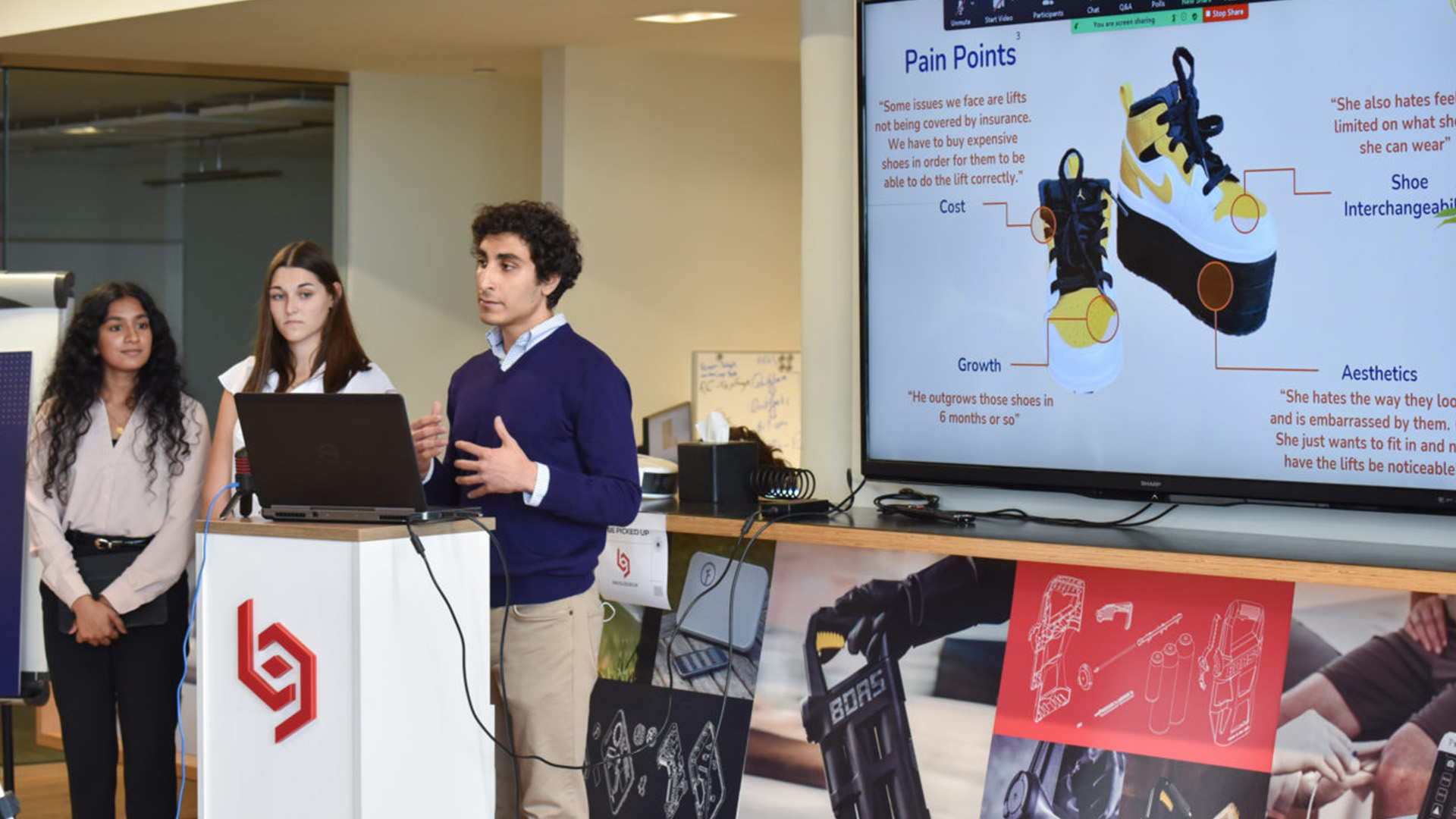 Team Soleia students stand at a podium presenting with a laptop while a screen behind them displays their custom shoe lift design concept.