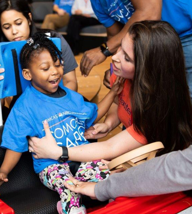 A group of students surround 4-year-old Ariel and assist her into the driver’s seat of the off-the-shelf toy Jeep they refined to meet her needs.