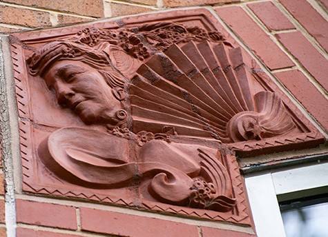 A person's face along with some ornate detailing sculpted on the outside of the building of the Paul J. Gutman Library.