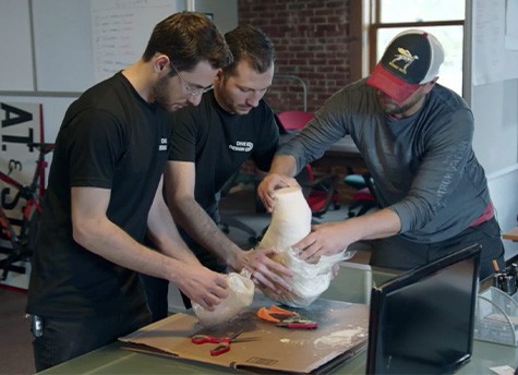 Adam Hecht, Alexander Thol, and Derrick Campana all stand around a table while holding and creating a prosthetic model together.