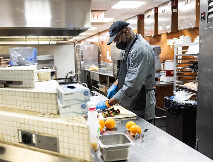 A food service worker at the Common Thread in the Kanbar Campus Center prepares food for a new app-based, carry-out system in a commercial kitchen while wearing personal protective equipment.