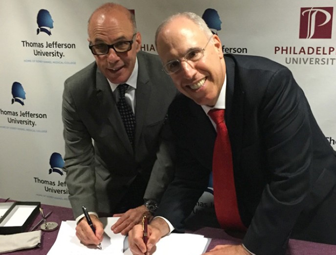University presidents Dr. Stephen Klasko (Thomas Jefferson) and Dr. Stephen Spinelli (Philadelphia) sign the merger agreement together in front of a step and repeat with both university logos.