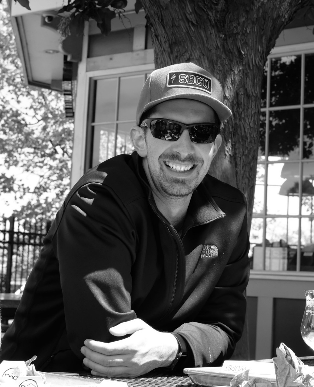 Black and white portrait of Eli Tuttle wearing a hat that says "SBCU" and sunglasses